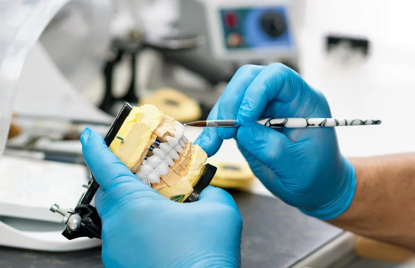 Dentista trabajando en un modelo dental con guantes azules, ajustando dientes posteriores para mejorar la función molar, clave en tratamientos de estética dental anterior en Clínica Gonzalvo.