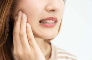 Mujer con dolor mandibular tocándose la zona de la ATM, síntoma asociado al desgaste dental severo