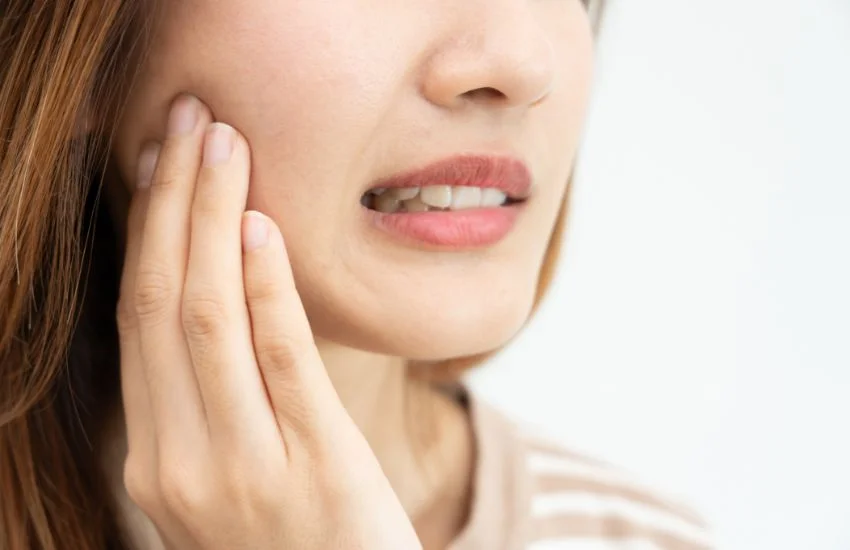 Mujer con dolor mandibular tocándose la zona de la ATM, síntoma asociado al desgaste dental severo
